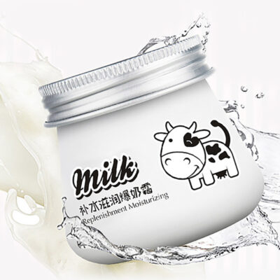 کرم شیر گاو ایباگ با بسته بندی سفید و درب نقرهای، دارای طرح گاو کارتونی و نوشتهی Milk روی ظرف، در پس زمینه پاشیده شدن شیر، نماد رطوبت رسانی و شادابی پوست.