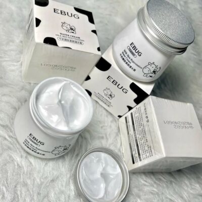 کرم شیر گاو ایباگ EBUG با بسته بندی سفید و طرح پوست گاو، حاوی کرم روشنکننده و آبرسان برای پوست صورت و بدن، نمایش با درب باز و بافت نرم و کرمی محصول